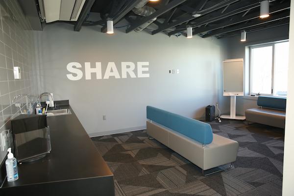 casual meeting space with two couches, kitchenette, note board, and windows facing street